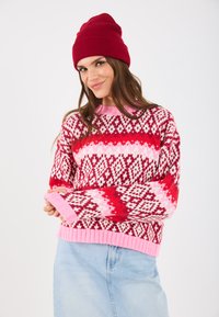 Sarkans un rozā rakstains džemperis ar dimanta un zigzaga rakstiem, ribotiem piedurknēm un apakšmalu. Saskaņots ar vienkrāsainu sarkanu beanie cepuri.