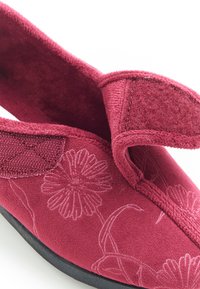 Rode stoffen slipper met bloemenborduurwerk, een klittenbandsluiting, een zachte textuur en een zwarte rubberen zool voor duurzaamheid.