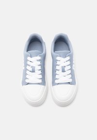 Ζεύγος ανοιχτόχρωμων γαλάζιων αθλητικών παπουτσιών με λευκά κορδόνια, λευκά λαστιχένια καλύμματα στα δάχτυλα και λευκές σόλες, σε απλό ανοιχτό γκρι φόντο.