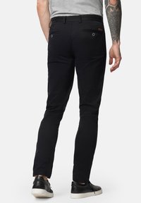 Czarne spodnie o slim fit, z tylnymi kieszeniami i elastycznym paskiem w talii. Noszone z czarnymi, teksturowanymi sneakersami.