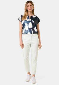Navy and white patterned short-sleeve top with a keyhole neckline, paired with white tapered pants and white sneakers. Smooth fabric texture.
