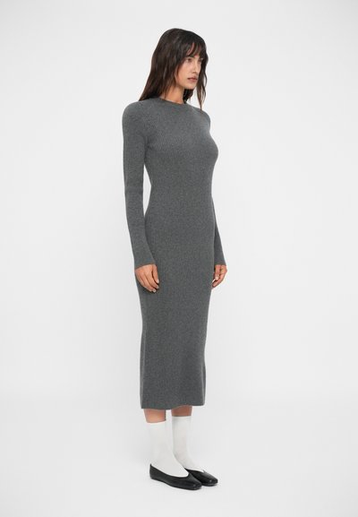 Robe en tricot côtelé gris avec manches longues, silhouette ajustée, longueur mi-mollet, portée avec des chaussettes blanches et des chaussures plates noires.