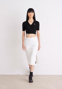 Čierny cropped top s krátkymi rukávmi, skombinovaný s bielou midi sukňou s bočným rozparkom. Obe odevy majú logové akcenty.