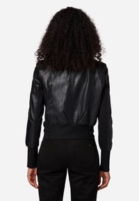 Černá kožená bombera s žebrovanými manžetami a lemem. Vyznačuje se hladkou texturou a přiléhavým střihem. Žádné viditelné kovové detaily.