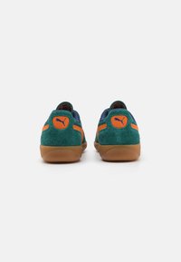 Adidași Puma cu partea superioară din suede verde, accente portocalii și detalii bleumarin; talpă din cauciuc cu adaos de gumă; design rotunjit și guler umplut.