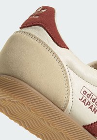 Bež i maroon tenisice od antilopa i kože, s reljefnom gumenom potplatom i bijelim šavovima. Imaju Adidasov logo na peti.