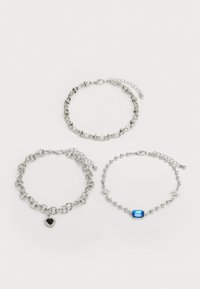 Three silver bracelets: one with a heart charm, one with a blue gem, and a third with star accents, featuring varying link designs.