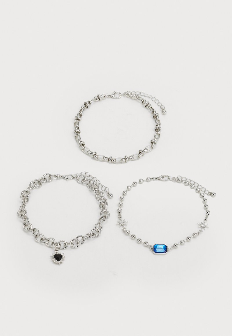 Three silver bracelets: one with a heart charm, one with a blue gem, and a third with star accents, featuring varying link designs.