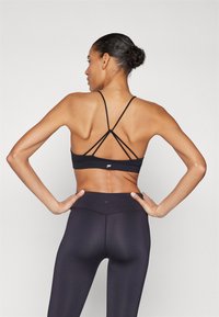Sujetador deportivo negro con tirantes cruzados en la espalda, combinado con leggings negros de cintura alta. El material parece suave y elástico, ofreciendo soporte.