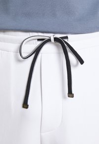 Pantalones deportivos blancos con un cordón en blanco y negro, que cuentan con una cinturilla texturizada y un pequeño acento metálico de marca.