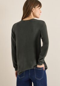 Ciemnozielona koszula z długim rękawem i okrągłym dekoltem, wykonana z miękkiego materiału. Charakteryzuje się luźnym fasonem i delikatnym przeszyciem z tyłu.