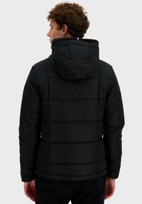 Veste matelassée noire avec des sections quiltées horizontales, une capuche et un petit accent tricolore au niveau du cou. Matériau doux avec une texture lisse.