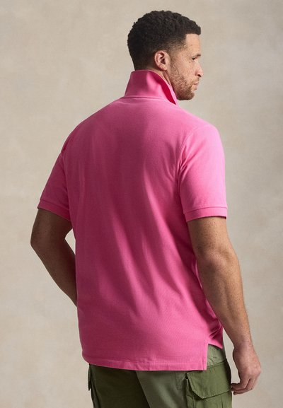 Ροζ πόλο πουκάμισο με όρθιο γιακά, κοντά μανίκια, πλαϊνές σχισμές και λείο ύφασμα, σε συνδυασμό με χακί cargo παντελόνι.