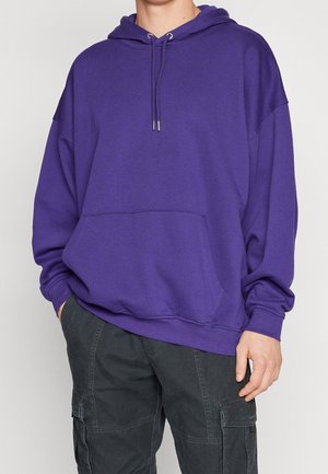 Felpa viola con cappuccio, tasca a marsupio, scollo con coulisse e vestibilità ampia. Realizzata in tessuto morbido con polsini a coste.