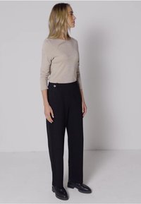 Pull en maille beige à manches longues, associé à un pantalon noir taille haute avec un détail de bouton sur le côté et des chaussures plates noires.