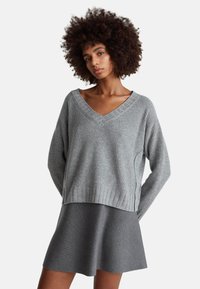 Grauer, gerippter Strickpullover mit V-Ausschnitt und langen Ärmeln, kombiniert mit einem grauen ausgestellten Rock, beide aus weichen Materialien.