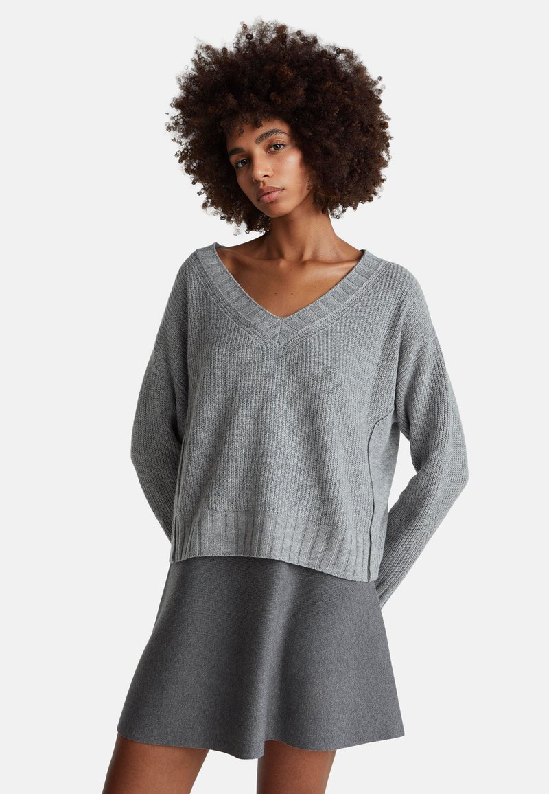 Grauer, gerippter Strickpullover mit V-Ausschnitt und langen Ärmeln, kombiniert mit einem grauen ausgestellten Rock, beide aus weichen Materialien.