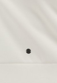 Tessuto bianco con una superficie liscia che presenta un piccolo logo ovale nero ricamato al centro, accentuato da dettagli argentati.