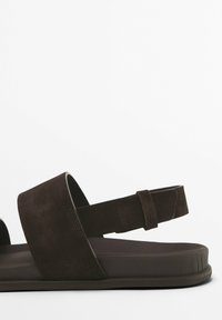 Bruna mockaskor med ett brett band över foten och ett bakband. Platt sula med en strukturerad yta, minimalistisk design.