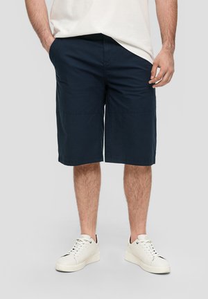 Shorts décontractés bleu marine à coupe ample, dotés de poches et d'une texture lisse, associés à des baskets blanches.