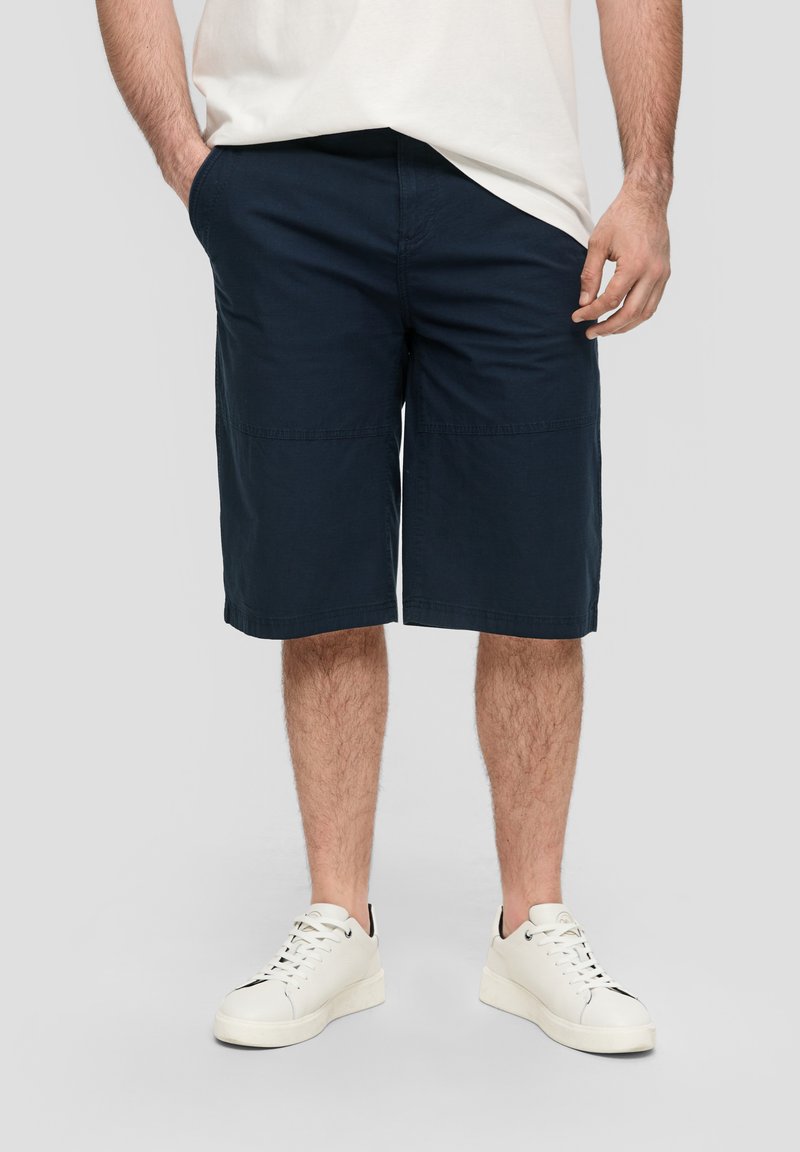 Shorts décontractés bleu marine à coupe ample, dotés de poches et d'une texture lisse, associés à des baskets blanches.
