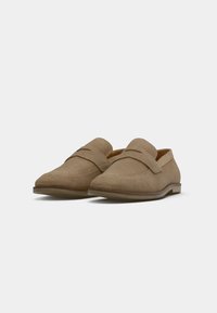 Beige Wildleder Slipper mit schlichtem Design, ausgestattet mit einer genähten Kappen und einem Mokassin-Obermaterial. Flache Gummisohle mit minimalem Profil.