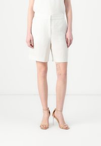Hvite linshorts med middels høy midje, med rett snitt og en teksturert overflate, kombinert med brune høye hæler.