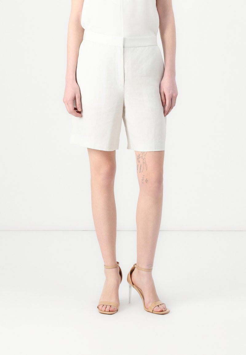 Hvite linshorts med middels høy midje, med rett snitt og en teksturert overflate, kombinert med brune høye hæler.