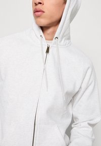 Weißer Zip-Hoodie mit einer vorderen Tasche, Kapuze mit Kordelzug und Raglanärmeln; verfügt über einen Metallreißverschluss und strukturierten Stoff.
