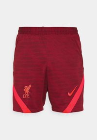 Punaiset urheilushortsit, joissa on teksturoitu kuvio. Shortsien sivussa on Liverpoolin FC:n logo ja kirkkaan oranssi Nike-swoosh.