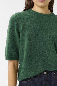Green wool sweater with short sleeves, a crew neckline, and a soft, textured finish. Paired with dark denim jeans and metal button details.