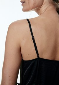Schwarzes Camisole mit dünnen verstellbaren Trägern, weichem Material und gerafftem Design am Saum. Glatter, minimalistische Rückansicht.