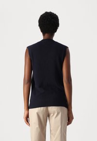 Maglione senza maniche di colore navy in morbido knit con orlo e spalle a coste. Abbinato a pantaloni beige chiaro, visto da dietro.