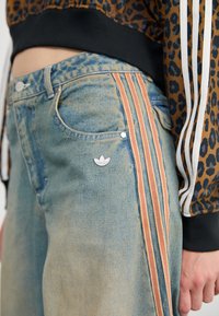 Denim jeans met een lichtblauwe wassing, voorzien van oranje en witte verticale strepen, zilveren hardware en een klein logo op de voorkant van de zak.