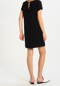 Robe noire à manches courtes avec une découpe en forme de clé au dos, fabriquée en tissu doux, présentant une coupe décontractée et une longueur au genou.