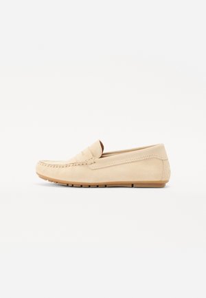 Mocassin en daim beige avec des détails cousus et une semelle en caoutchouc plate. Design à profil bas sans lacets ni accents métalliques visibles.