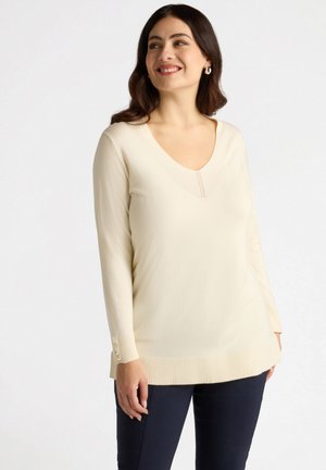 Suéter crema de cuello en V en suave tejido de punto, con puños acanalados que cuentan con detalles de botones y un dobladillo más largo a los lados para un estilo añadido.