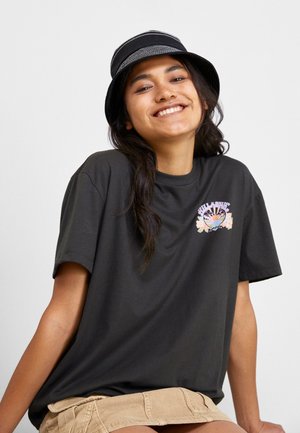 Black oversized t-shirt with short sleeves, featuring a colorful floral graphic on the chest. Paired with a beige corduroy skirt and black bucket hat.