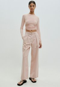 Helles rosa geripptes Langarm-Crop-Top mit seitlichen Bändern, kombiniert mit hochtaillierten, weiten Hosen. Flache schwarze Flip-Flops runden den Look ab.