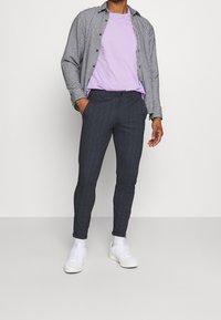 Svart och vit rutigt skjorta över en ljuslila t-shirt, matchad med mörka tajta byxor och vita sneakers. Slätt tyg med en figurnära design.