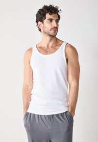 Un débardeur en coton blanc avec de larges bretelles, au design ajusté et à la texture lisse, associé à un short gris à cordon de serrage.