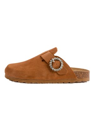 Sabot en suède marron avec un bout arrondi, une sangle ajustable et une boucle décorative en strass. Semelle en liège avec une traction texturée.