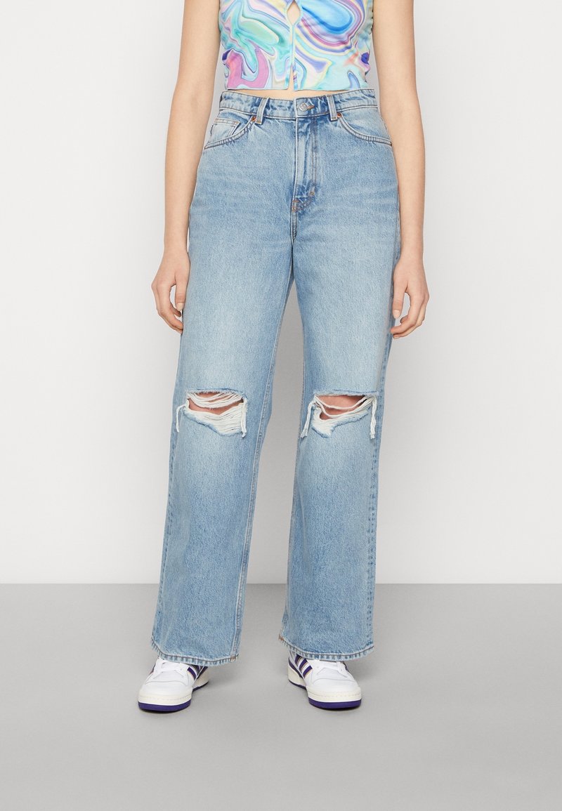 Ljusblå, vida denimjeans med slitna knän, fem fickor och hög midja. Materialet verkar mjukt med en blekt yta.