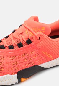 Scarpa sportiva di un vivace corallo con accenti neri e gialli, tomaia in rete, suola bianca maculata e marchio "XTRAIN" sulla linguetta e sul lato.