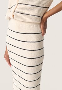 Costum format din două piese din tricot, de culoare crem, cu dungi bleumarin. Include o fustă ajustată și un top lejer cu textură corduroy și margine detaliată.