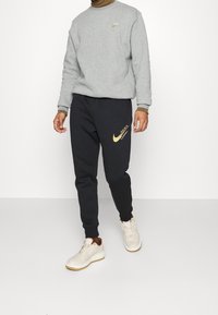 Gray sweatshirt with ribbed cuffs, black joggers featuring a gold Nike logo, and beige sneakers with brown accents.