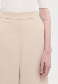 Pantaloni beige a gamba larga realizzati in tessuto morbido, con una vita piatta e dettagli di piega discreti, abbinati a una maglietta bianca a costine.