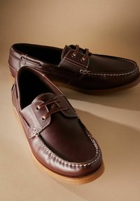 Braune Lederbootsschuhe mit kontrastierenden Nähten und Schnürdesign, die eine runde Zehenform und eine Sohle aus Gummi haben.