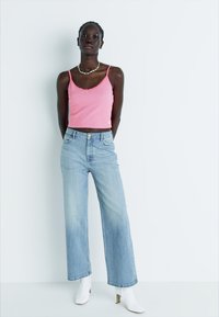 Ružičasti rebrasti crop top, svijetloplave široke traperice i bijele gležnjače. Značajne karakteristike uključuju suptilni izrez i opušteni kroj.