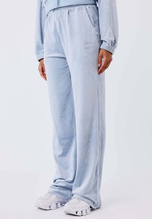 Pantaloni in velluto celeste con vita elasticizzata e decorazioni a forma di stella argentata, indossati con scarpe sportive bianche e top abbinato.